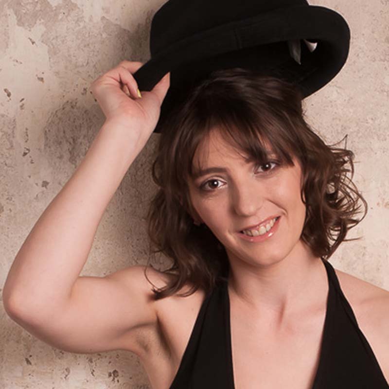Claudia zieht den schwarzen Hut, ihre Haare sind gestylt und leicht gelockt. Das Gesicht ist dezent geschminckt. Fotografiert von Michael Ruess
